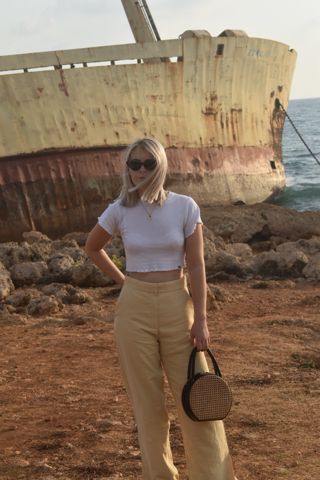 ILHA black Francesca handbag held by model, beach and boat in background