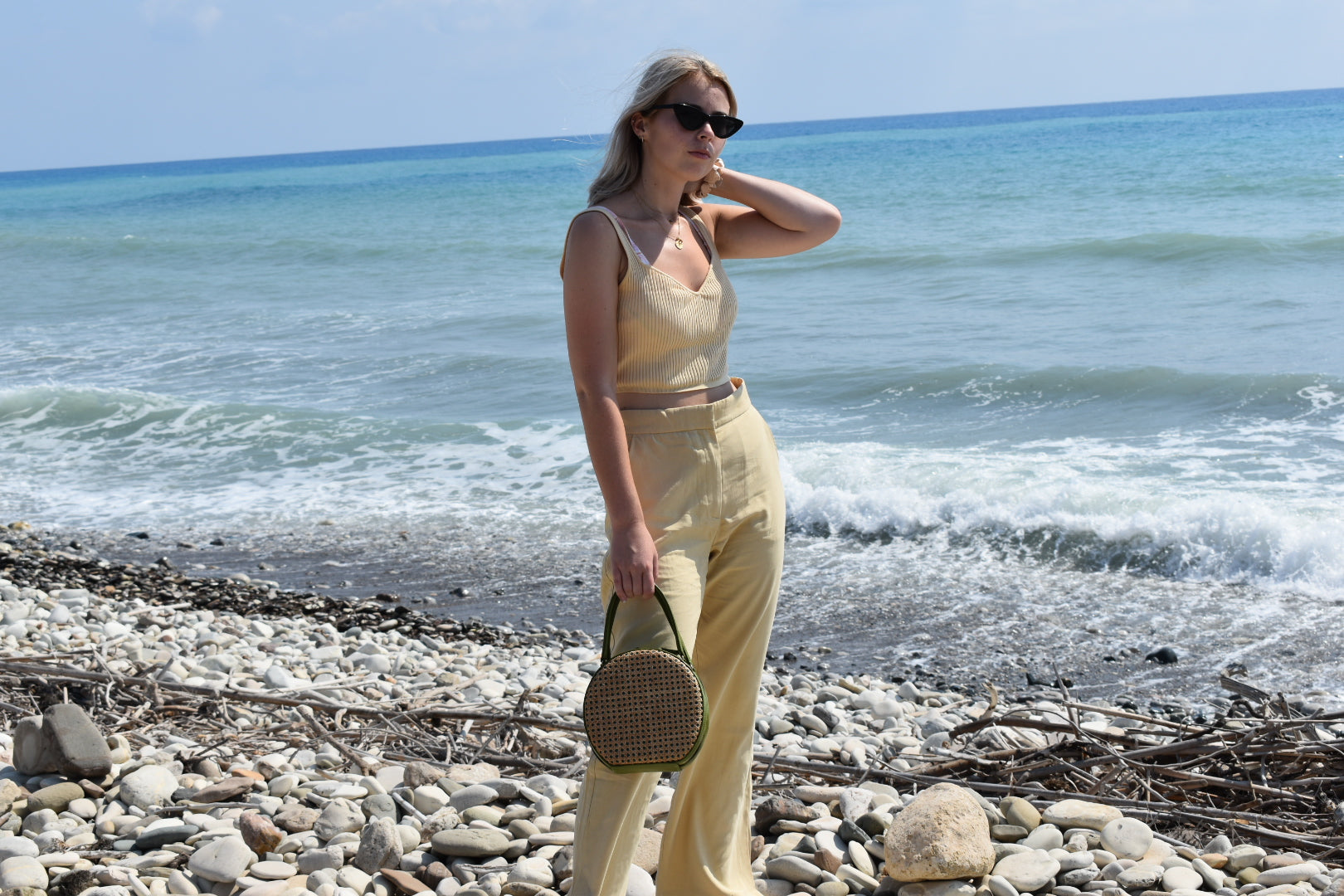 Model holds ILHA Francesca bag, Olive, on beach.