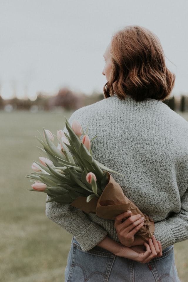 Woman holding flowers behind her back. 
