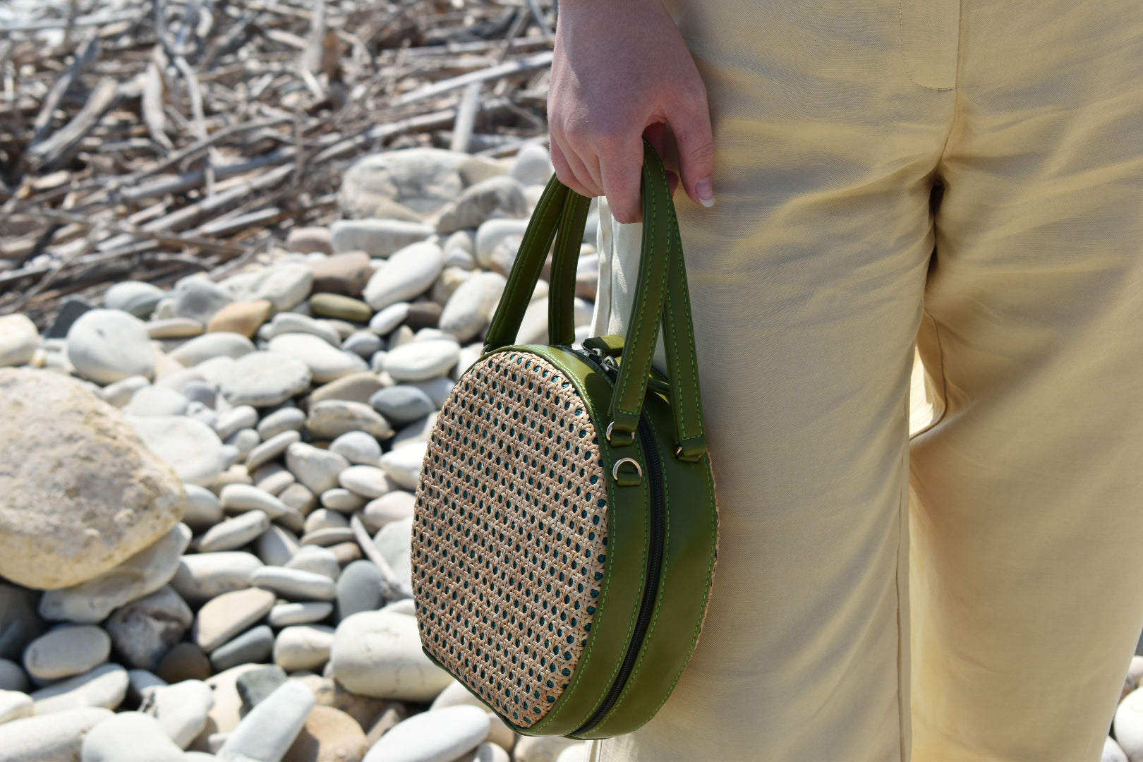 ILHA Francesca purse, Olive, held by model against white pebbles