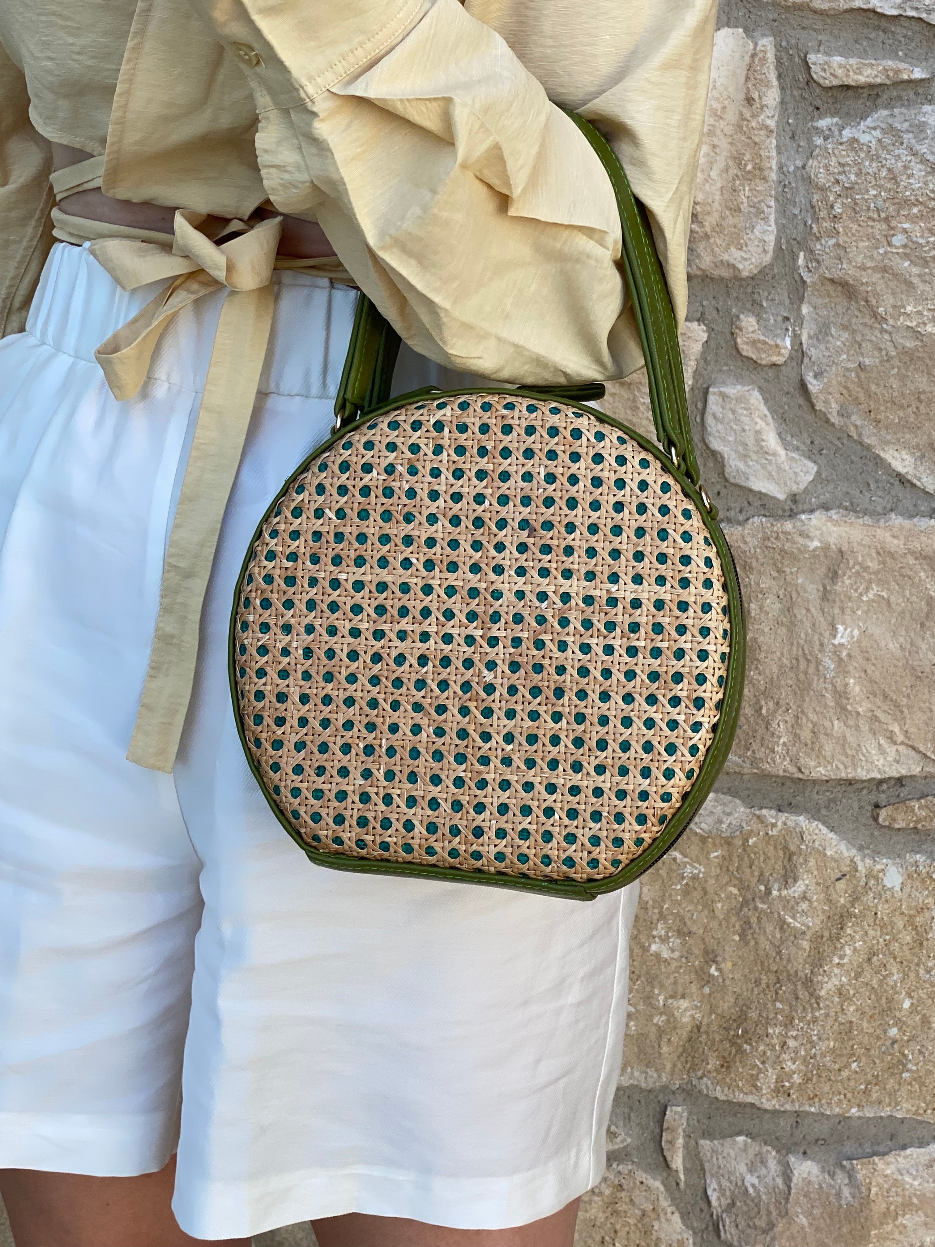 ILHA Francesca crossbody raffia bag, Olive, held by model against sandstone wall